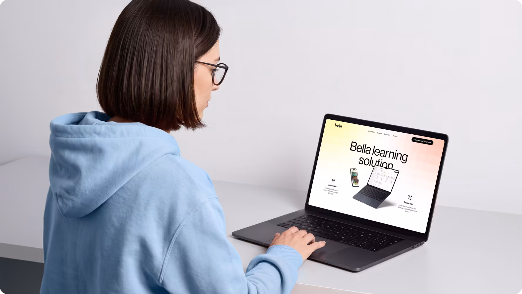 Woman in a hoodie browsing the Bella learning solution website on a laptop