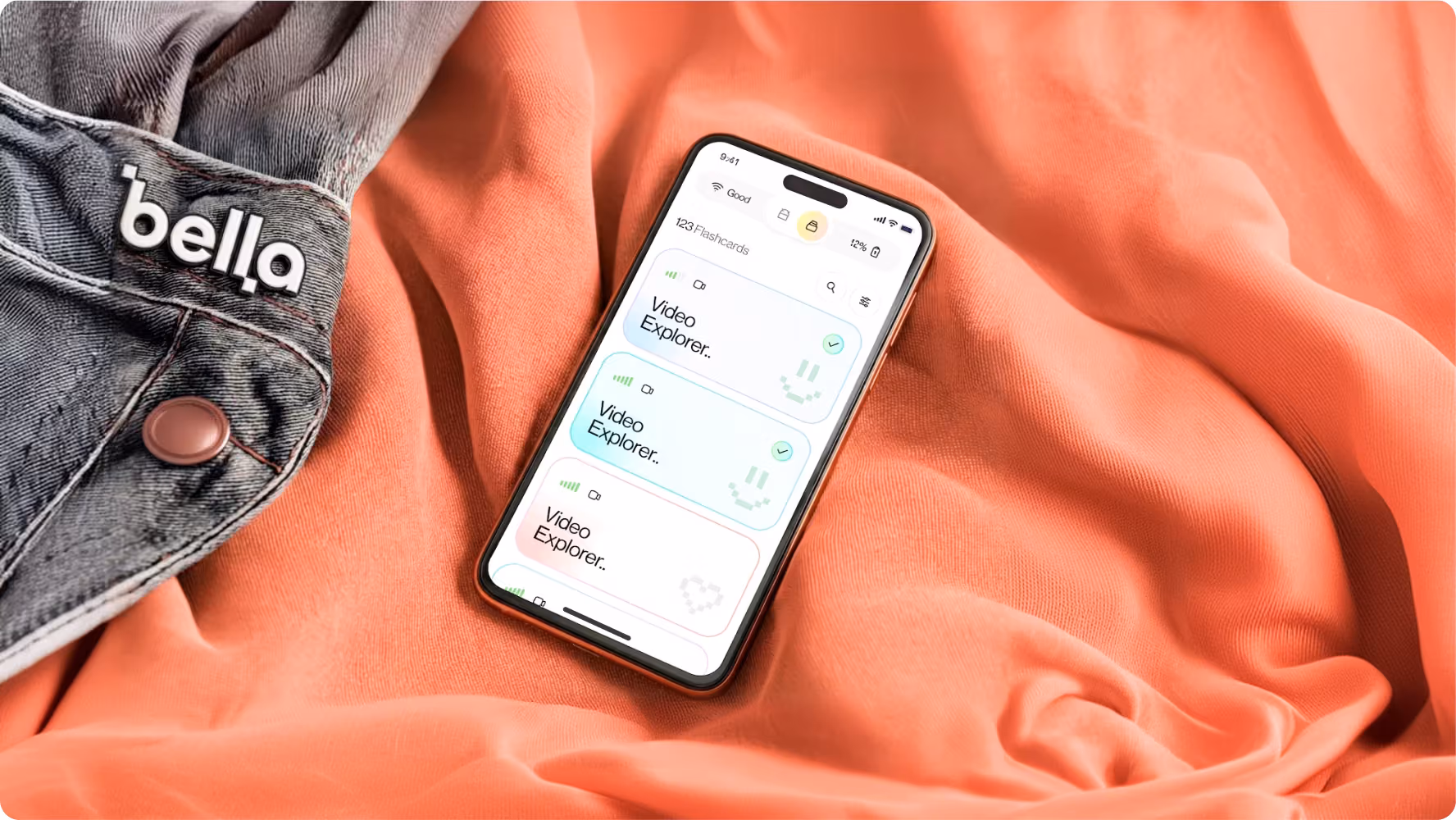 Bella app lesson list with Video Explorer tasks on a smartphone next to branded denim, designed by Halo Lab