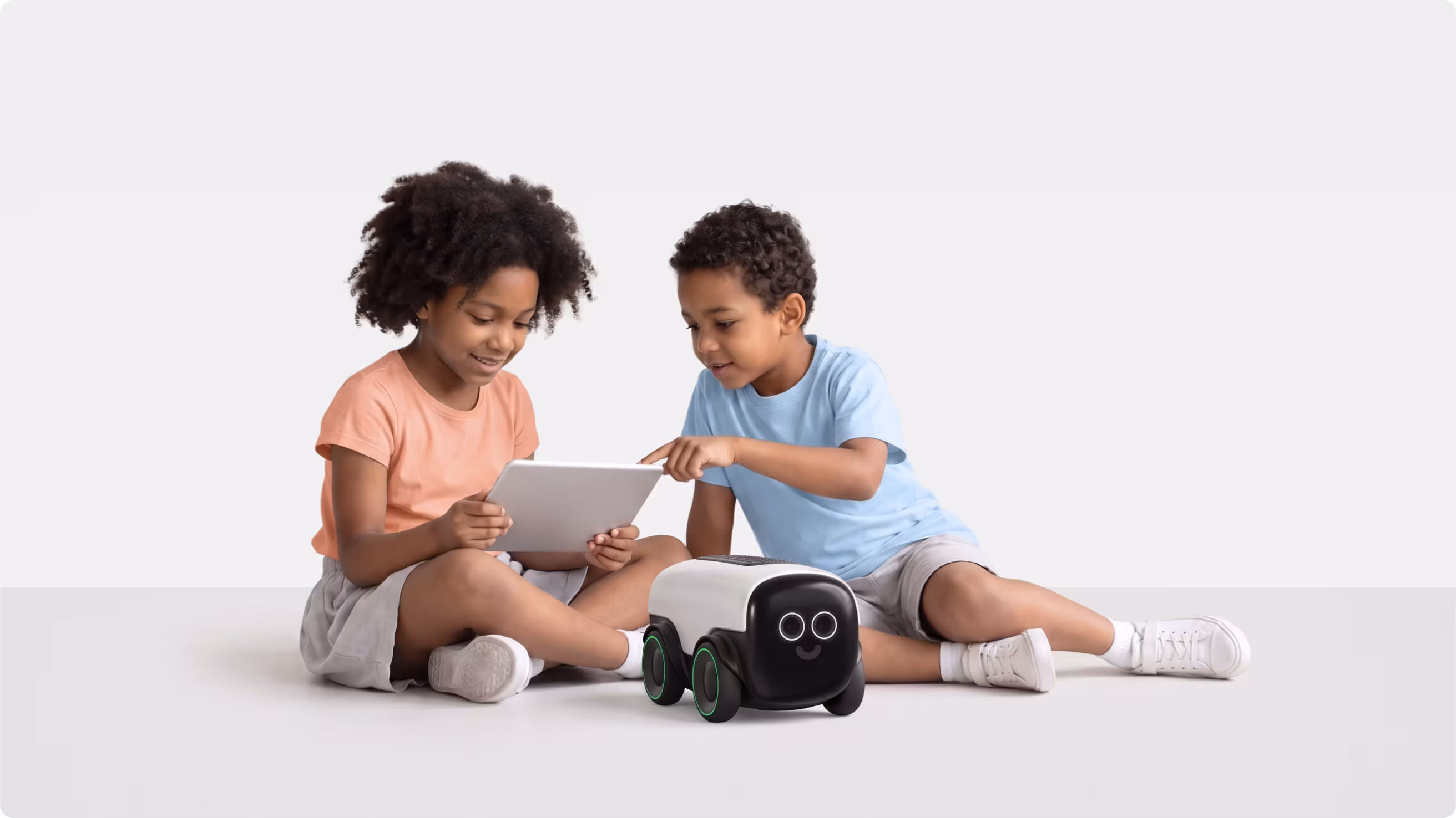 Two children using a tablet next to the Bella learning robot on the floor